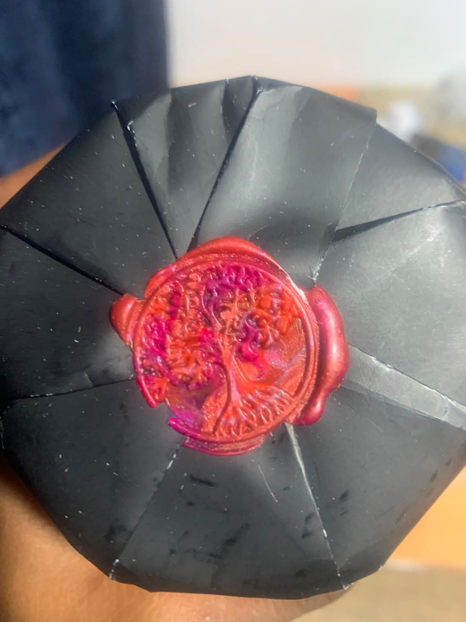 A tree crest pressed into red wax, sealing the folded black wrapping of a Wick-ed parcel.